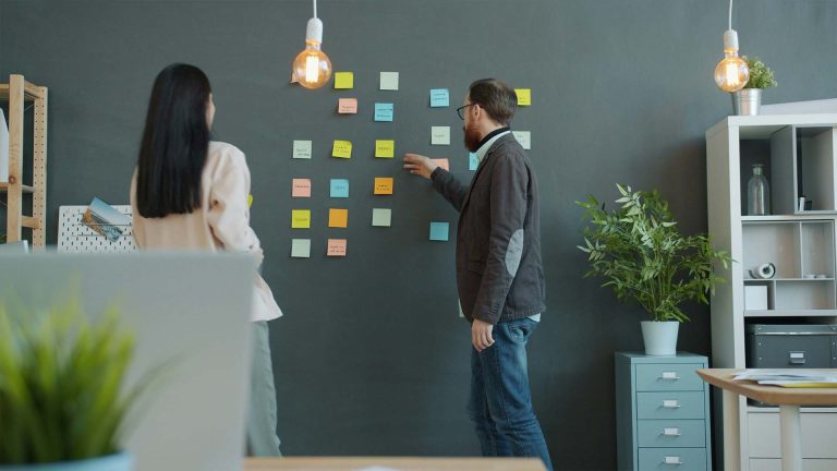 Two people with sticky notes on a wall in meeting